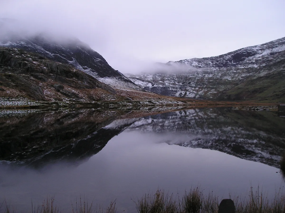 Misty mountain lake (Llyn Cwmorthin) reflecting snow-capped cliffs in Snowdonia, north Wales.