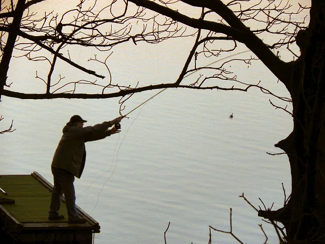 An angler fishing the bank of Wallsuches Reservoir, home of Curley's Trout Fishery, Horwich, Greater Manchester.