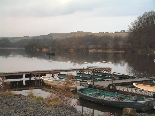 An angler fly fishing from a small boat near the pier on Lindores Loch