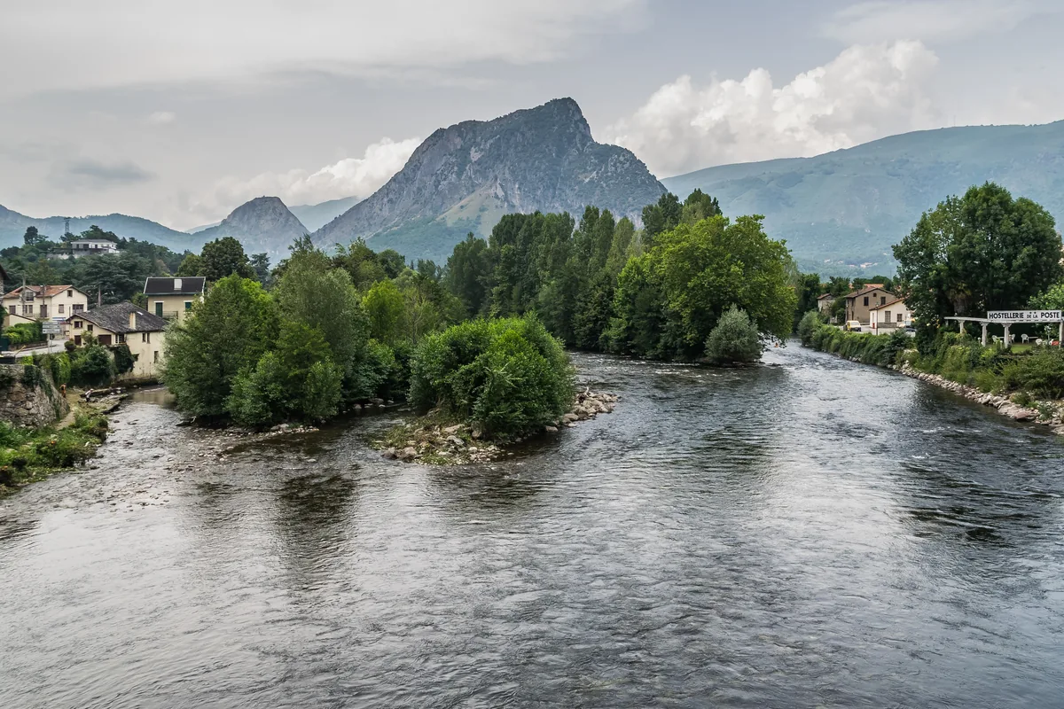 The Ariège River flowing through the town of Tarascon-sur-Ariège in the French Pyrenees, with a rocky peak rising behind the rooftops.