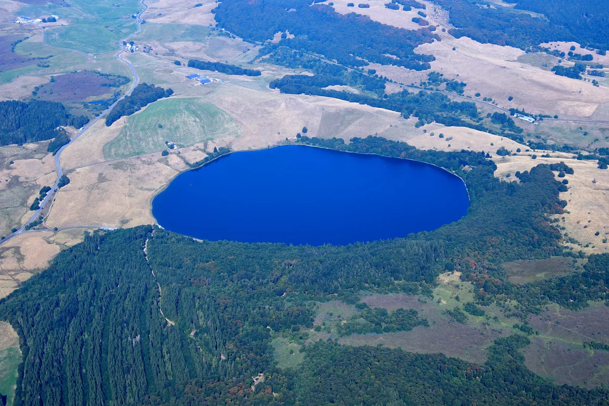Aerial view of the round volcanic Lac Chauvet surrounded by forest and farmland in the Monts Dore, Puy-de-Dôme, France