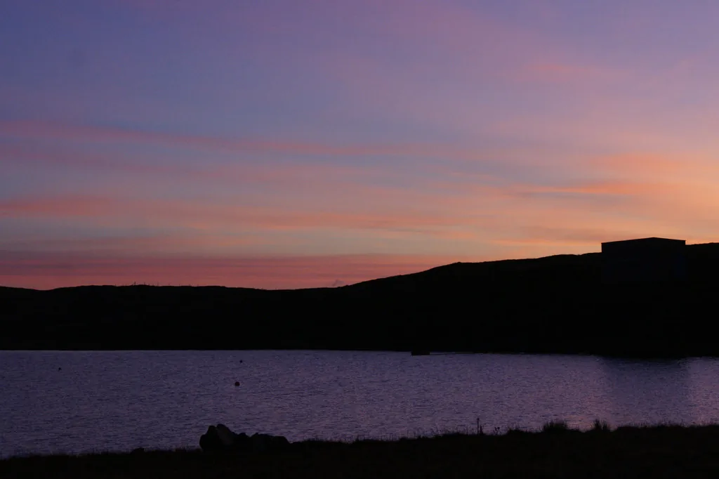 A calm Shetland loch, Lunga Water, near West Sandwick on the island of Yell, lit by dusk light.