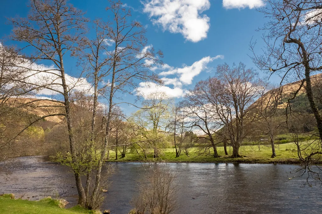 The River Lyon winding past trees and green fields, with the hills of Glen Lyon rising on either side.