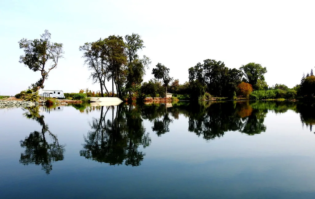 Still water on the Mokelumne River near Lodi, California, with trees and a small boat reflected on the surface.