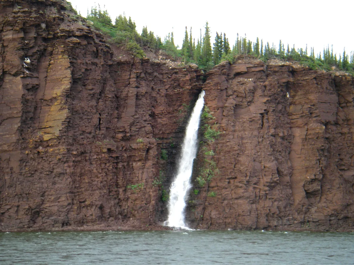 Small waterfall cascading over dark cliffs into the Coppermine River, boreal spruce forest along the rim, Nunavut/Northwest Territories Arctic barrens