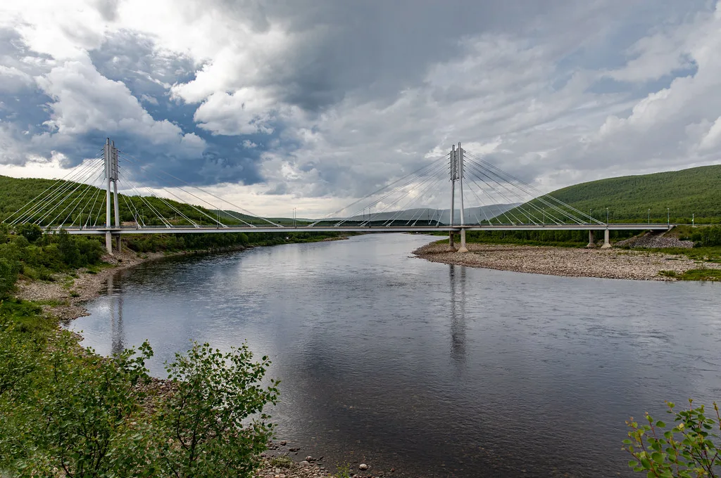 A wide clear river flowing under a modern cable-stayed bridge with gravel bars and green hills either side.