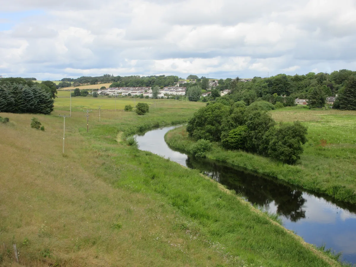 A meandering stretch of the River Ythan flowing through lush green pasture with trees along the banks near Ellon.