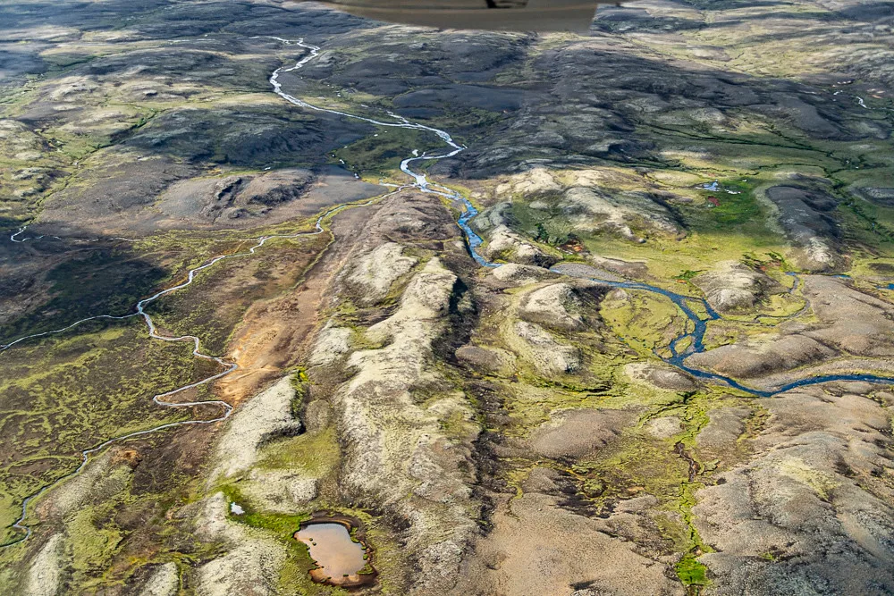 Aerial view of the Stora-Laxa river winding as a blue ribbon through green and grey volcanic lava-field terrain in Iceland.
