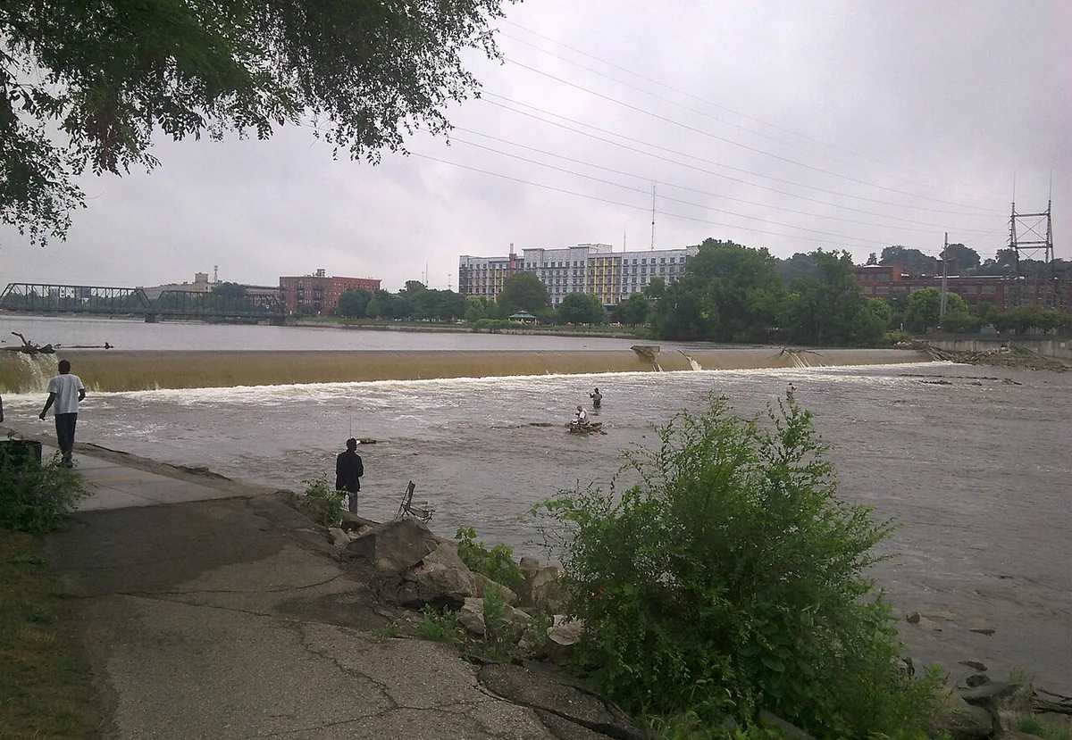 Wide view of the Grand River flowing over a low dam in downtown Grand Rapids, Michigan, with anglers wading in the current