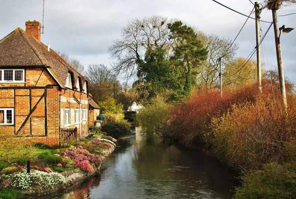 A clear chalk-stream channel of the River Lambourn running beside a red-brick cottage garden in East Garston village.