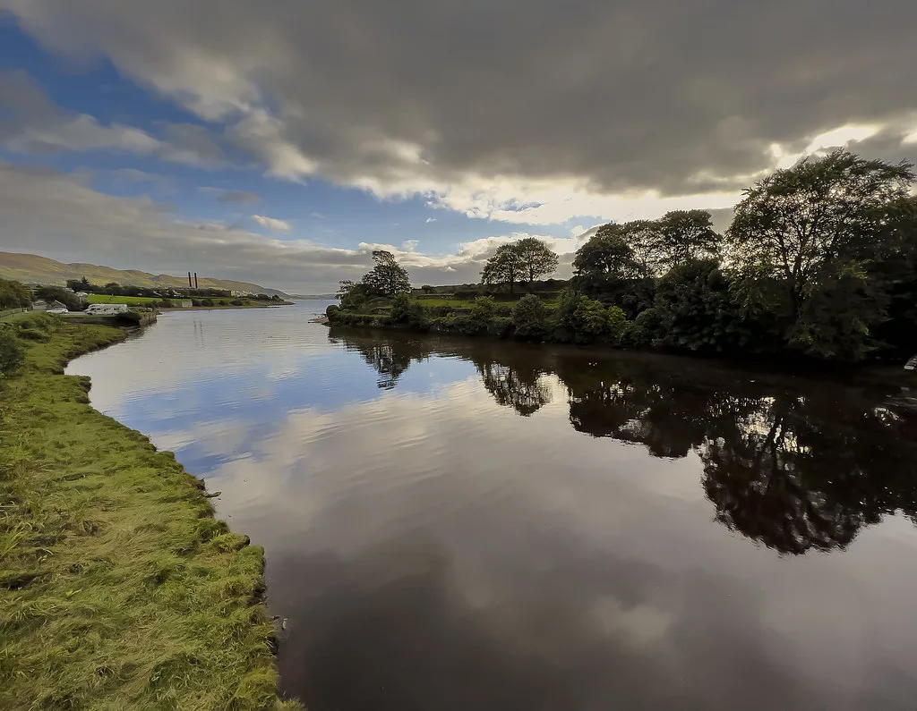 Still, dark water of the Crana River reflecting trees and sky near Buncrana, Co. Donegal, Ireland.