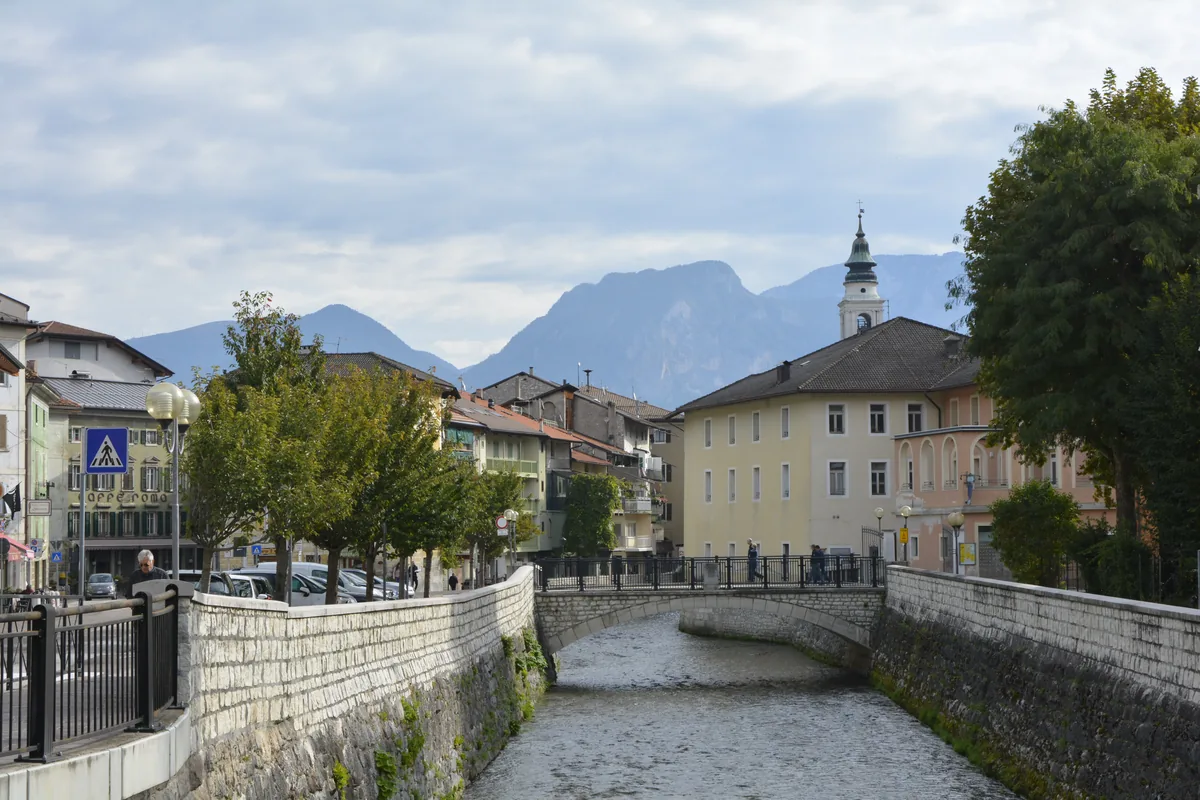 The Brenta river running through the historic centre of Borgo Valsugana with Alpine peaks and a bell tower in the background