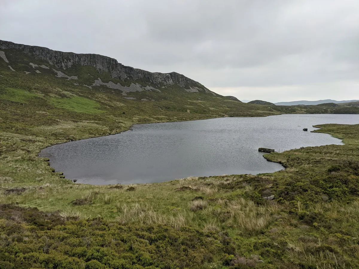 Upland lake (Llyn Gamallt Fawr) in Snowdonia with a rocky crag rising behind the far shore.