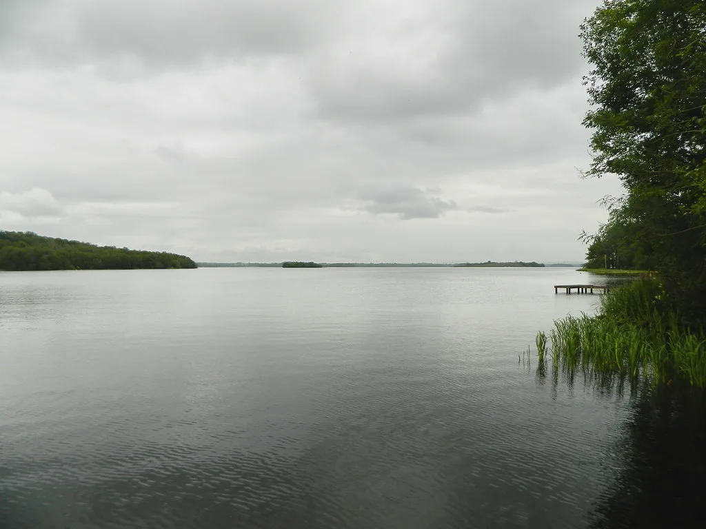 Calm, wide expanse of Lower Lough Erne under a cloudy sky, with wooded shoreline and a small jetty.