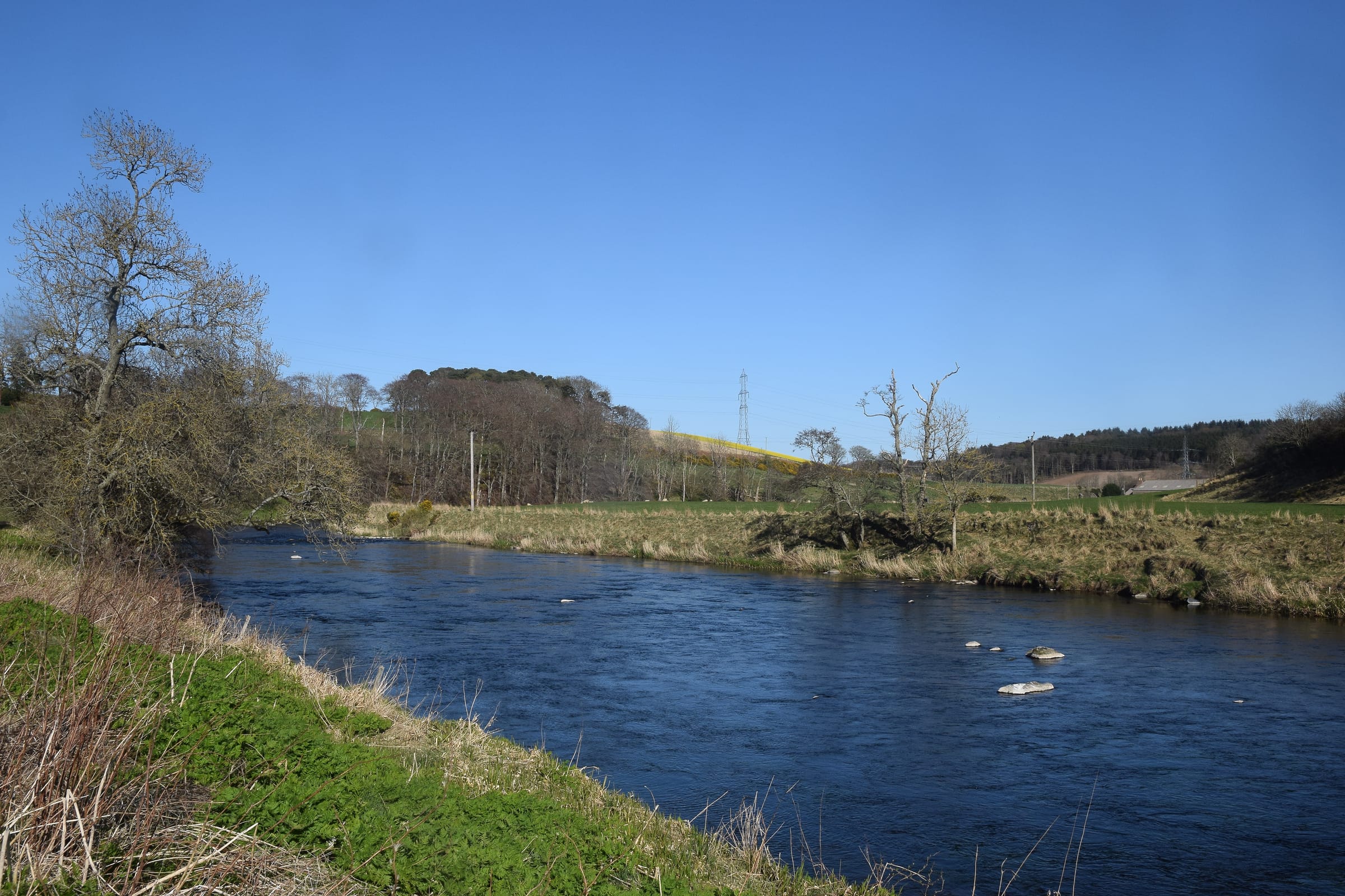 The River Don flowing serenely through agricultural land near Inverurie, Aberdeenshire, in early spring.