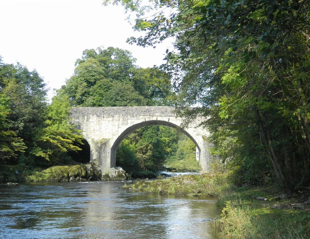 Historic stone arch bridge spanning the Border Esk river near Langholm, Dumfries and Galloway, with fast-flowing water and wooded banks