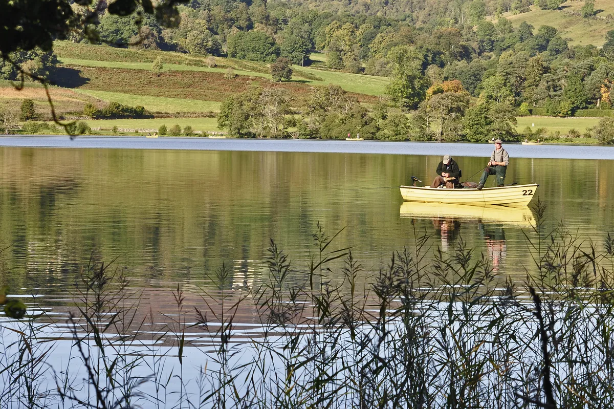 Two anglers fishing from a boat on the calm waters of Butterstone Loch with wooded hills behind