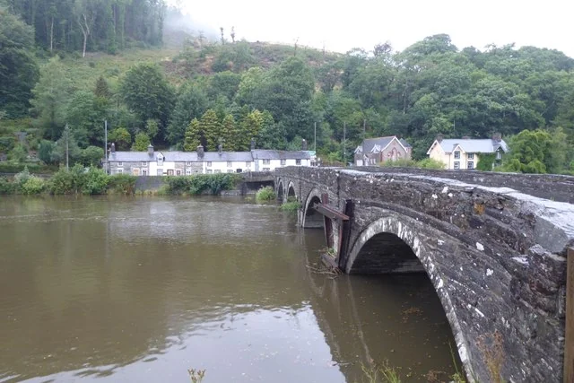 A stone bridge crossing the River Dovey (Afon Dyfi) at Machynlleth, with wooded hills behind.