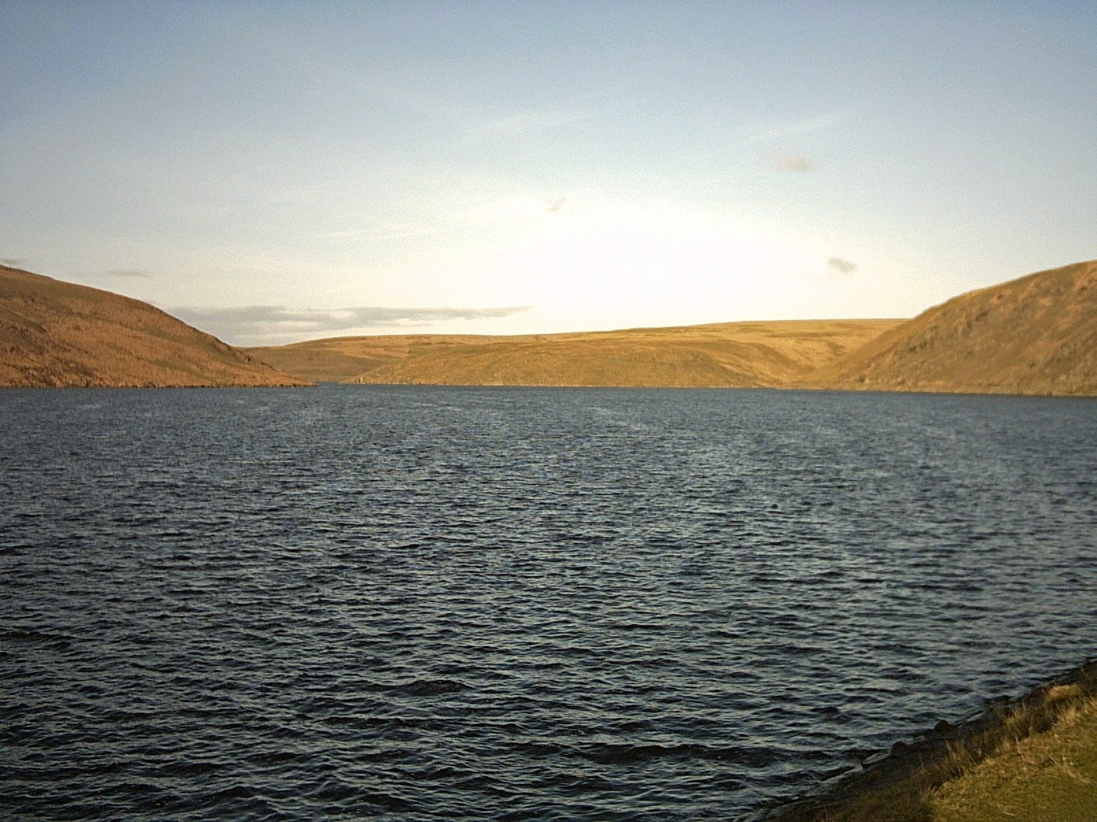 Claerwen Reservoir with its surrounding mountain ridges reflected in still water.