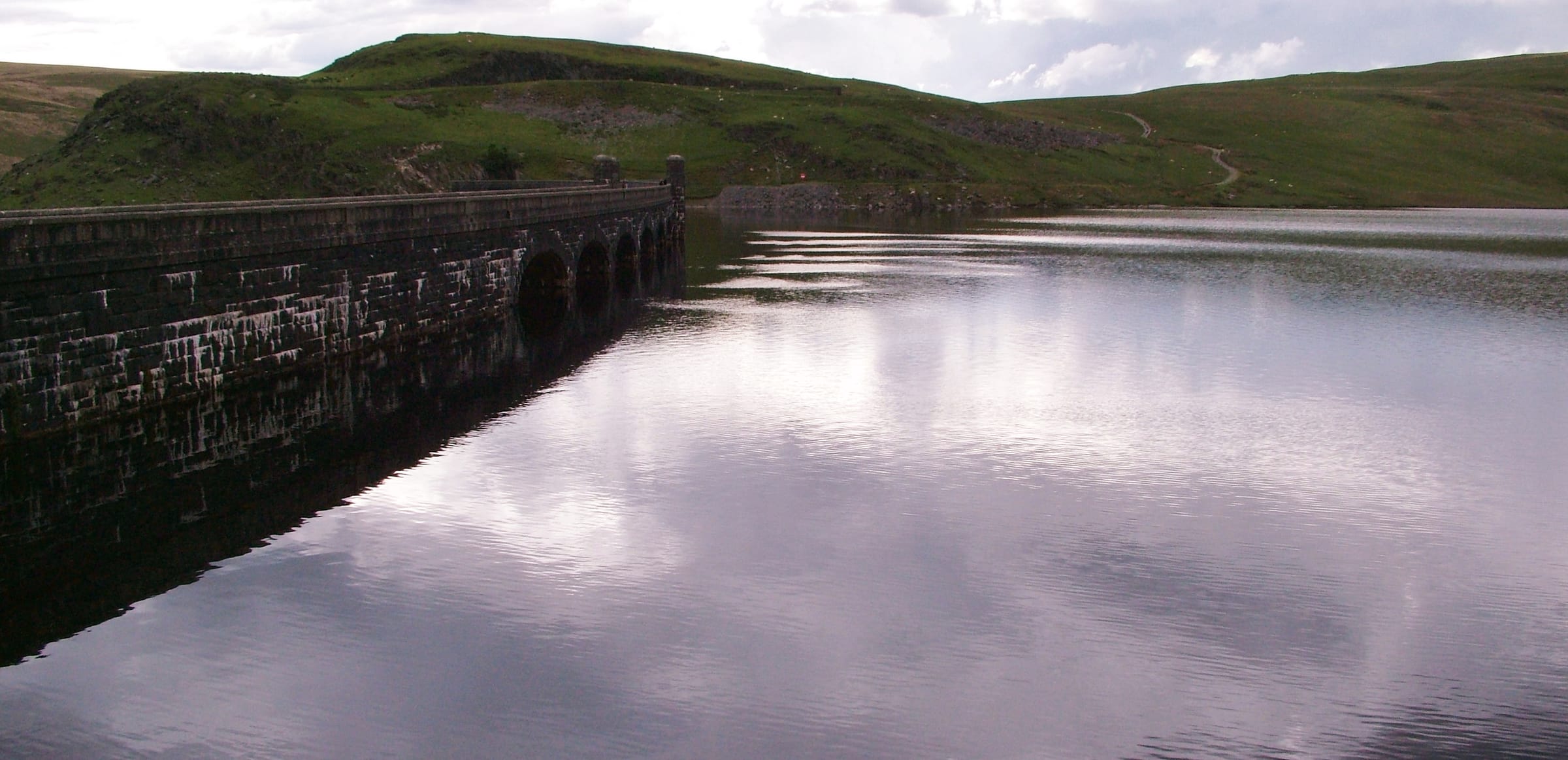Claerwen Reservoir in calm conditions, a wide panorama of still water stretching into the Cambrian uplands.