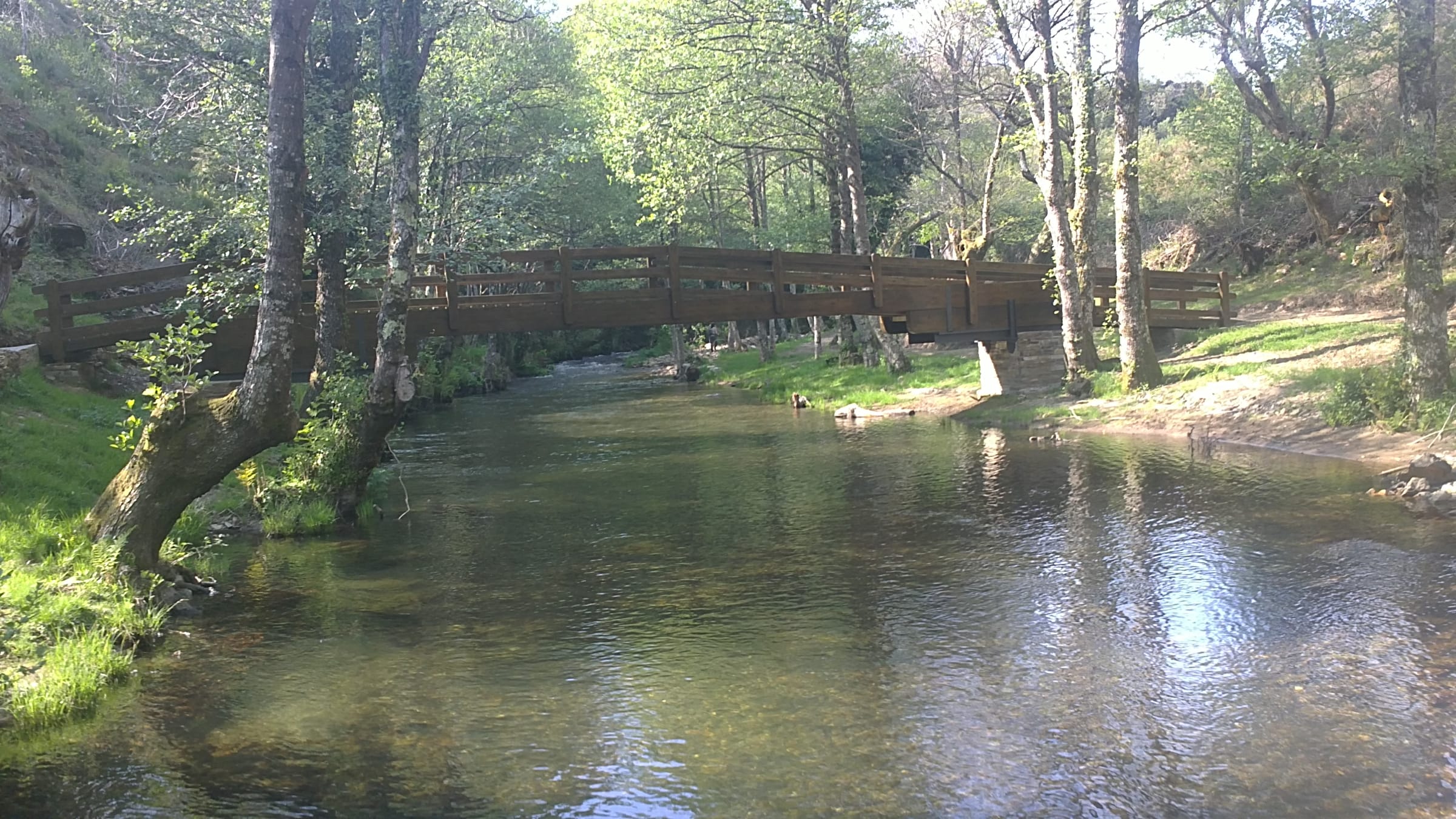 The Eo at the Cortevella recreational area in Baleira, Galicia, with a footbridge and riparian woodland.