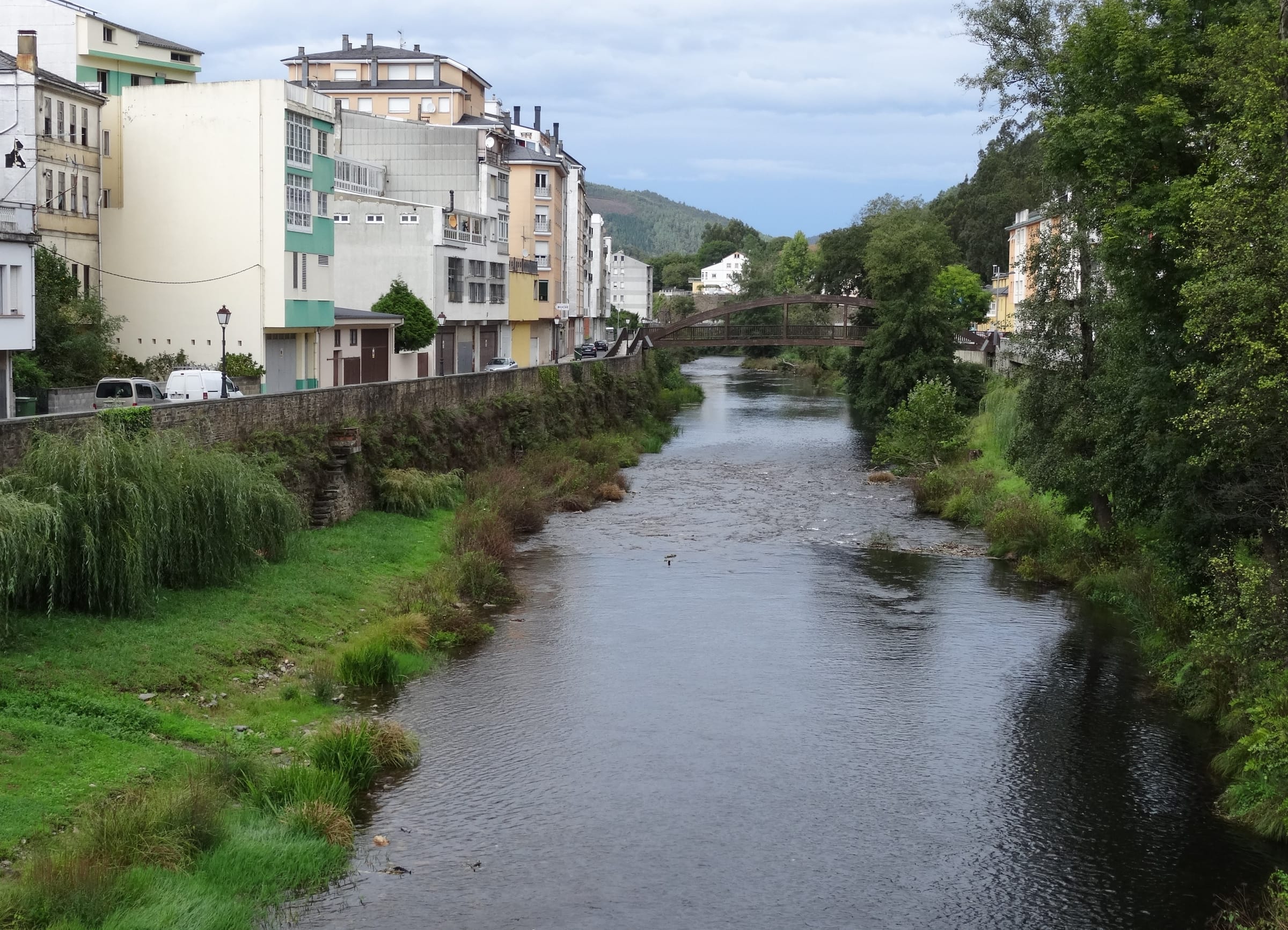 The Eo flowing through A Pontenova, Galicia, with wooded valley banks in autumn light.