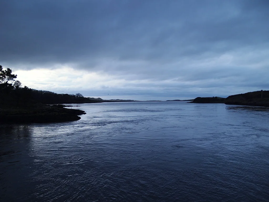 Wide, calm tidal waters of the River Erne estuary at Ballyshannon, Co. Donegal, Ireland, under a moody dusk sky.