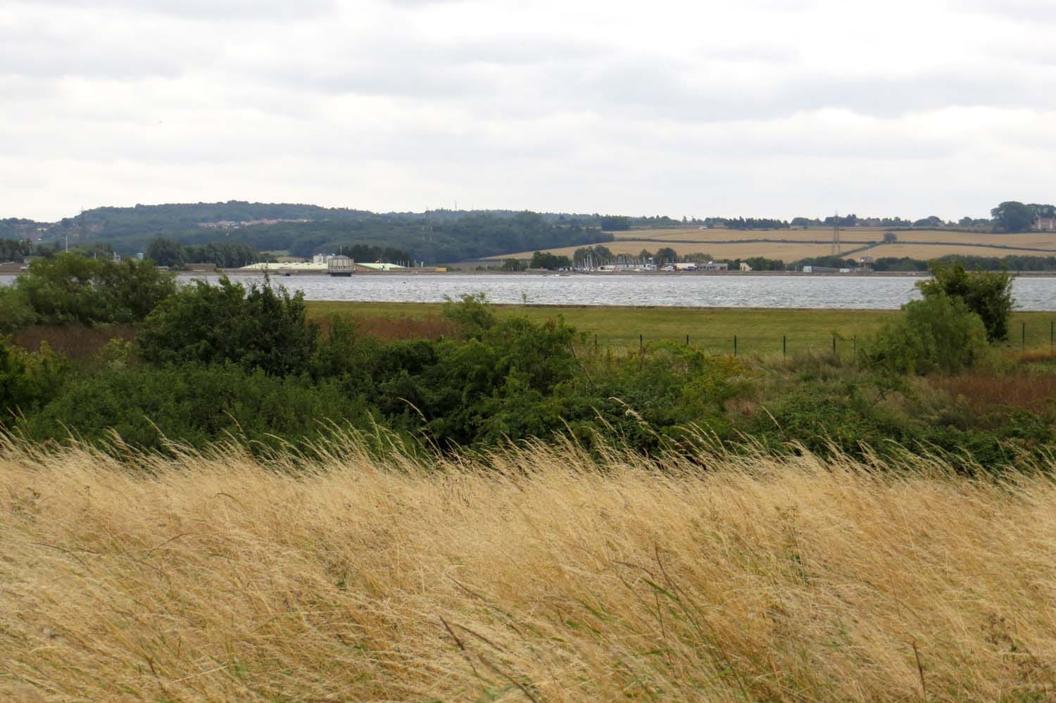 Open water expanse of Farmoor Reservoir viewed from the northern bank with the far shore and sky.