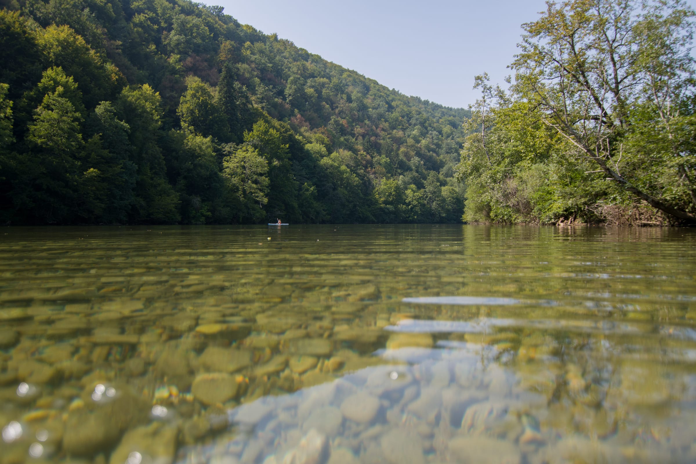 Water-level view of the crystal-clear Kolpa showing the pebble riverbed beneath shallow green water.