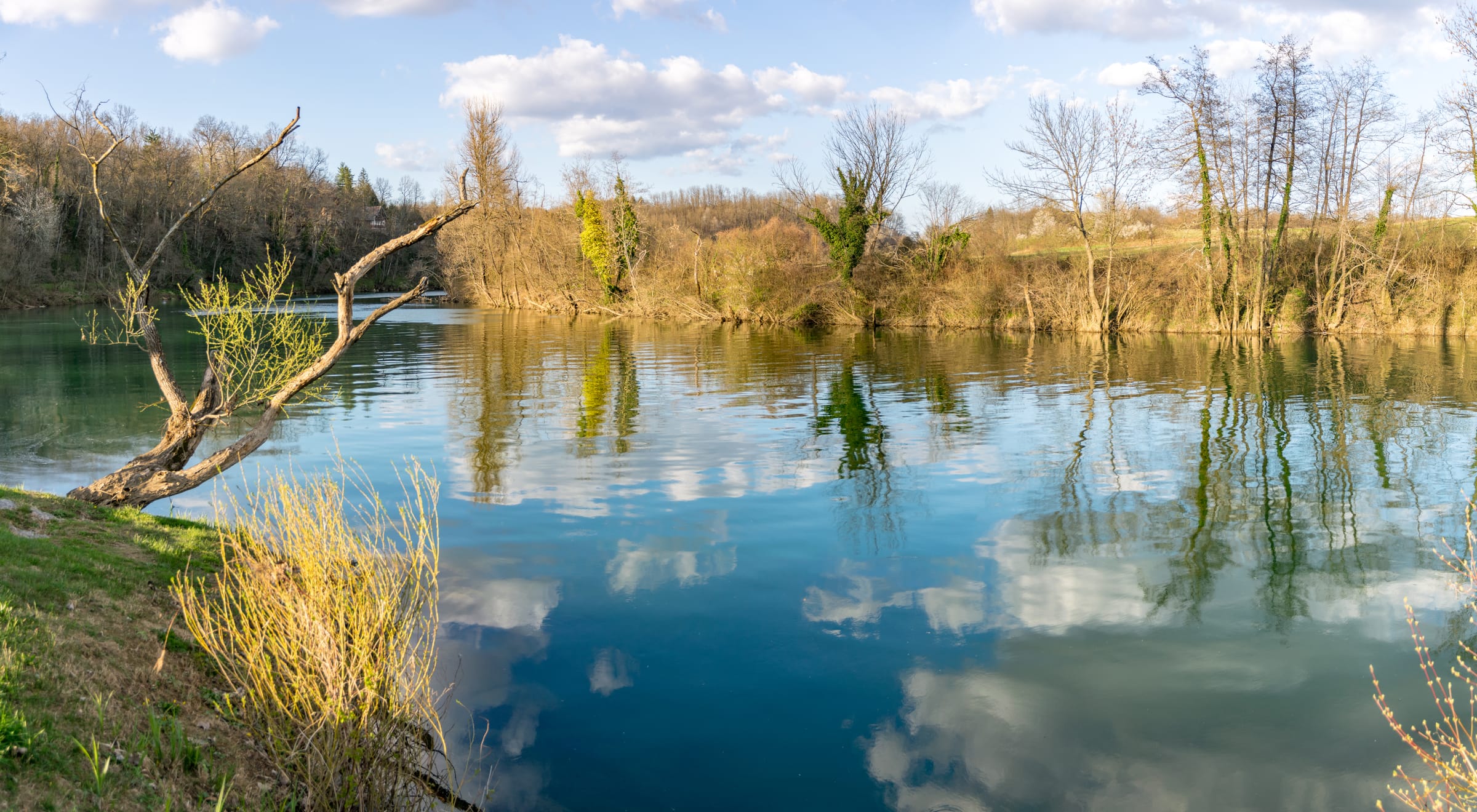 Calm blue Kolpa at Primostek reflecting clouds and riparian trees at the confluence with the Lahinja.