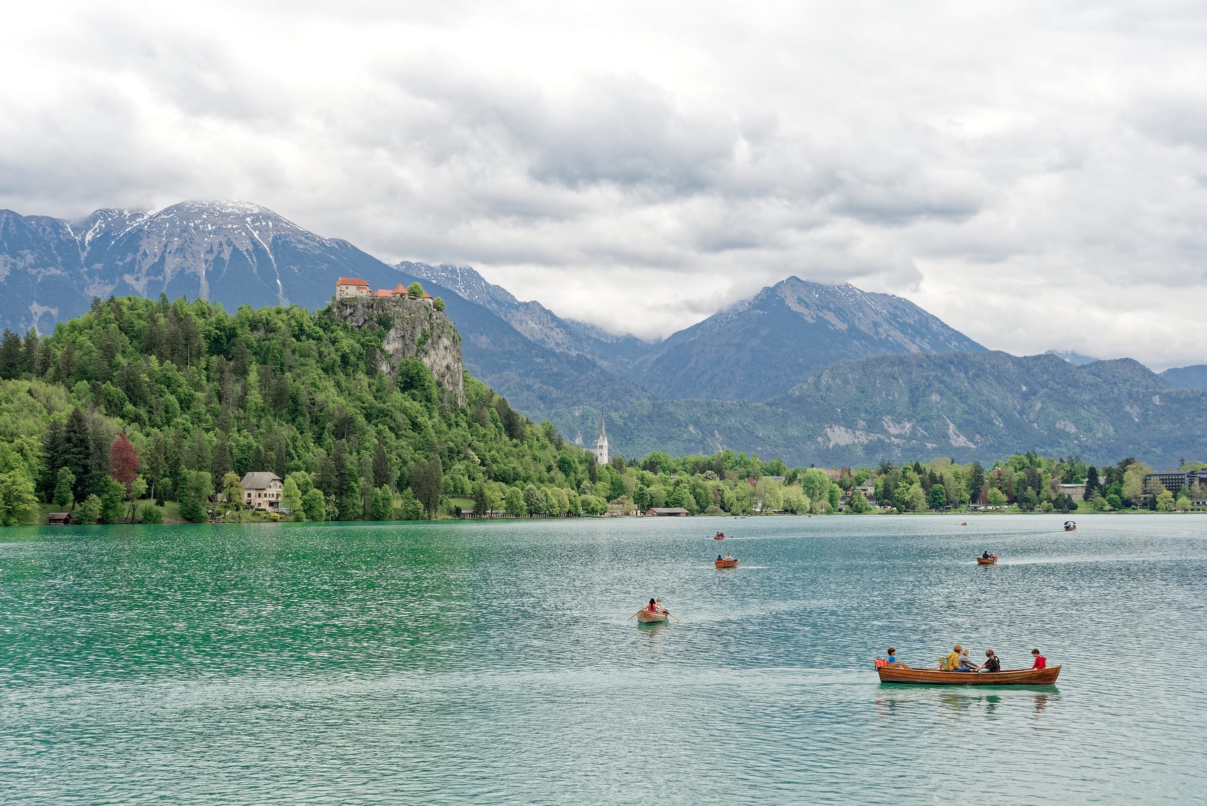 Wide shoreline view of Lake Bled with the lake in the foreground and Bled Castle on the cliff above the far shore.