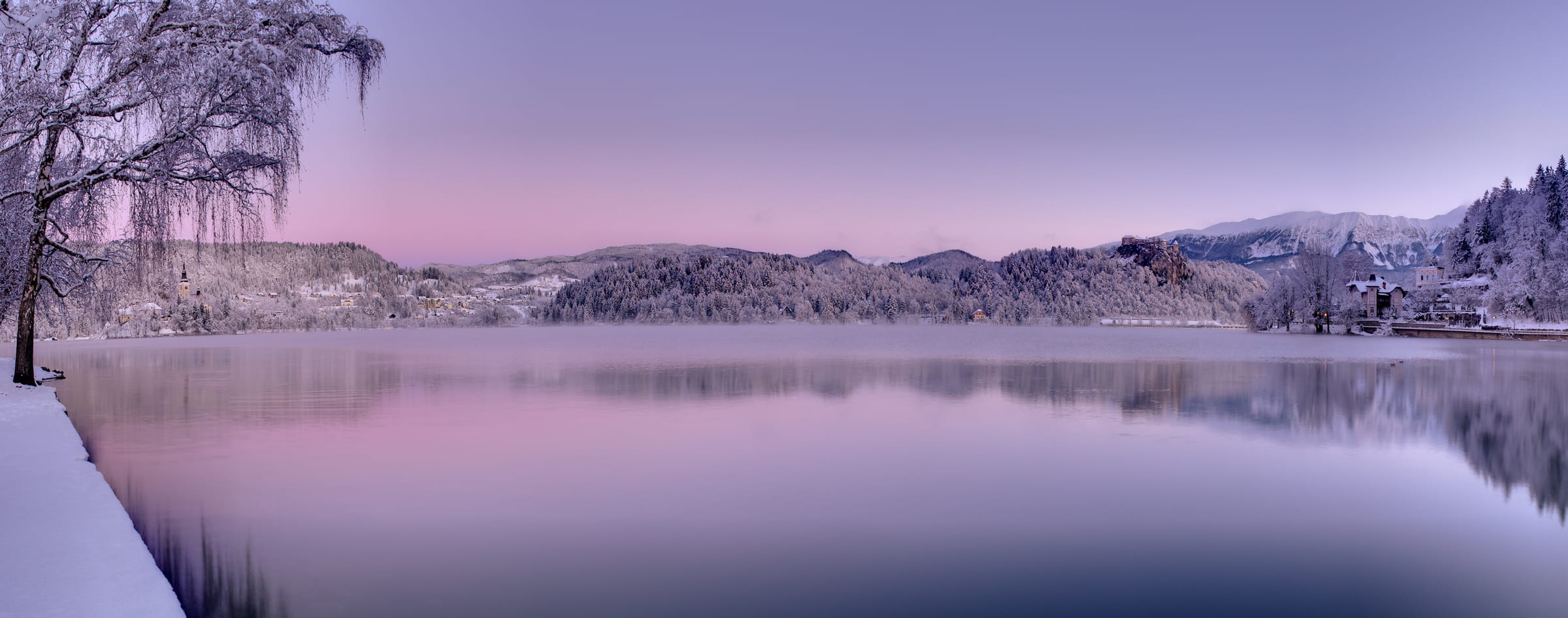 Wide panoramic view of Lake Bled showing the full lake basin, the island church, hillsides and the Julian Alps.