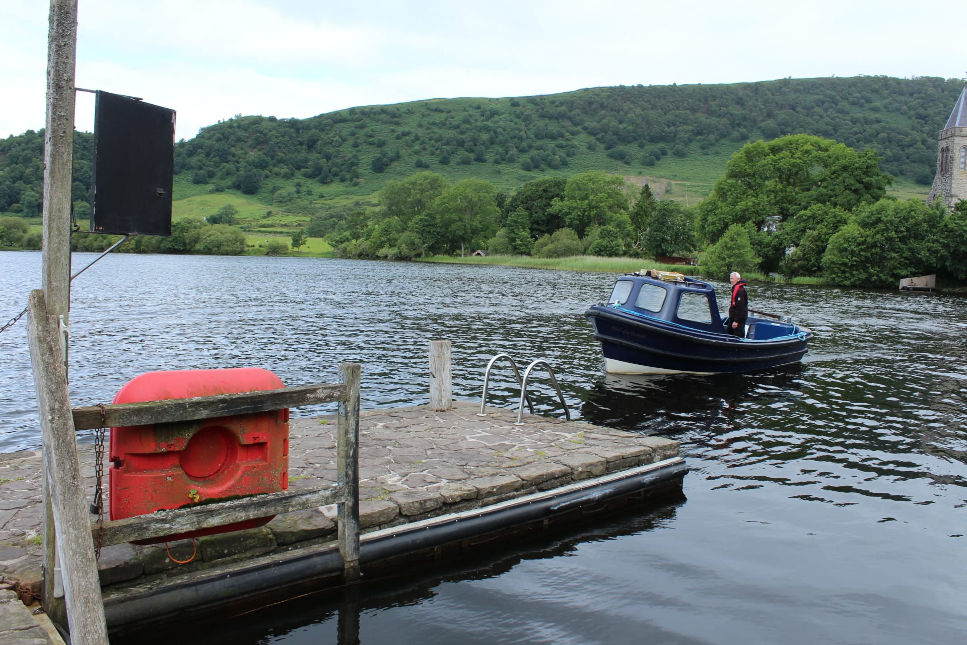 Wooden jetty at the Port of Menteith with the Inchmahome ferry on the open lake, tree-lined shoreline behind.