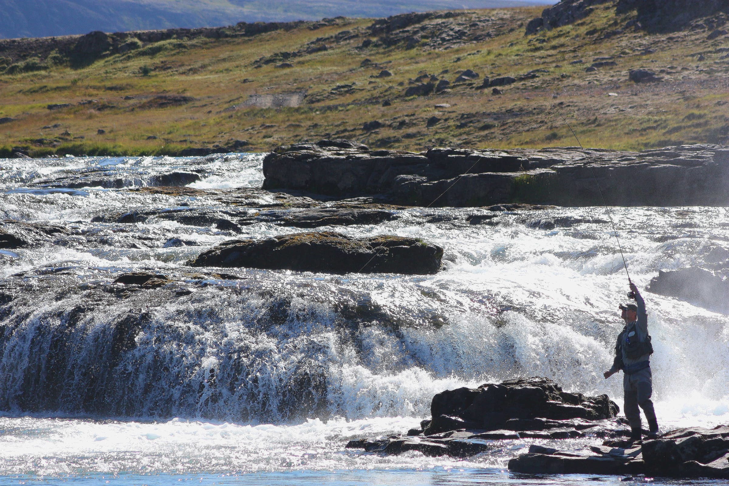 A fly fisher wading a boulder-strewn rapid on the Laxá í Kjós salmon river, Iceland.