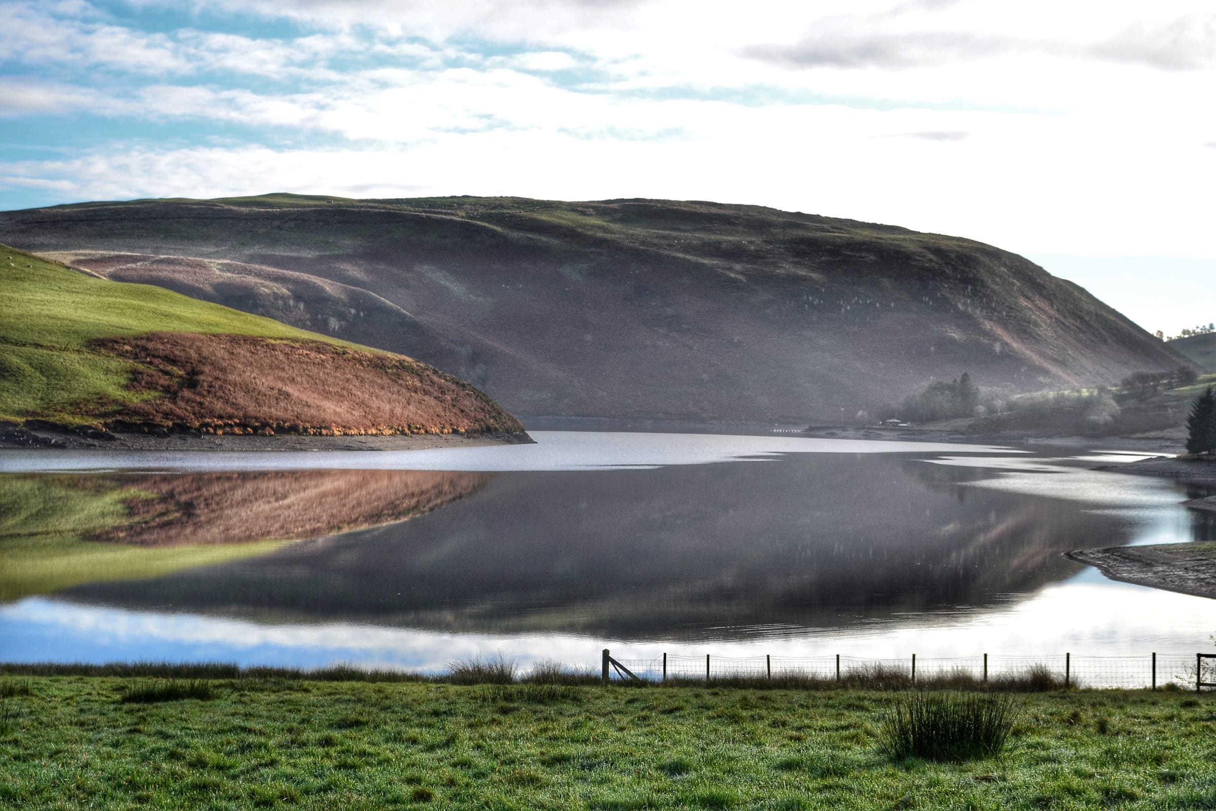 Clywedog dam with vivid reflections of autumn colour in the still reservoir water below.