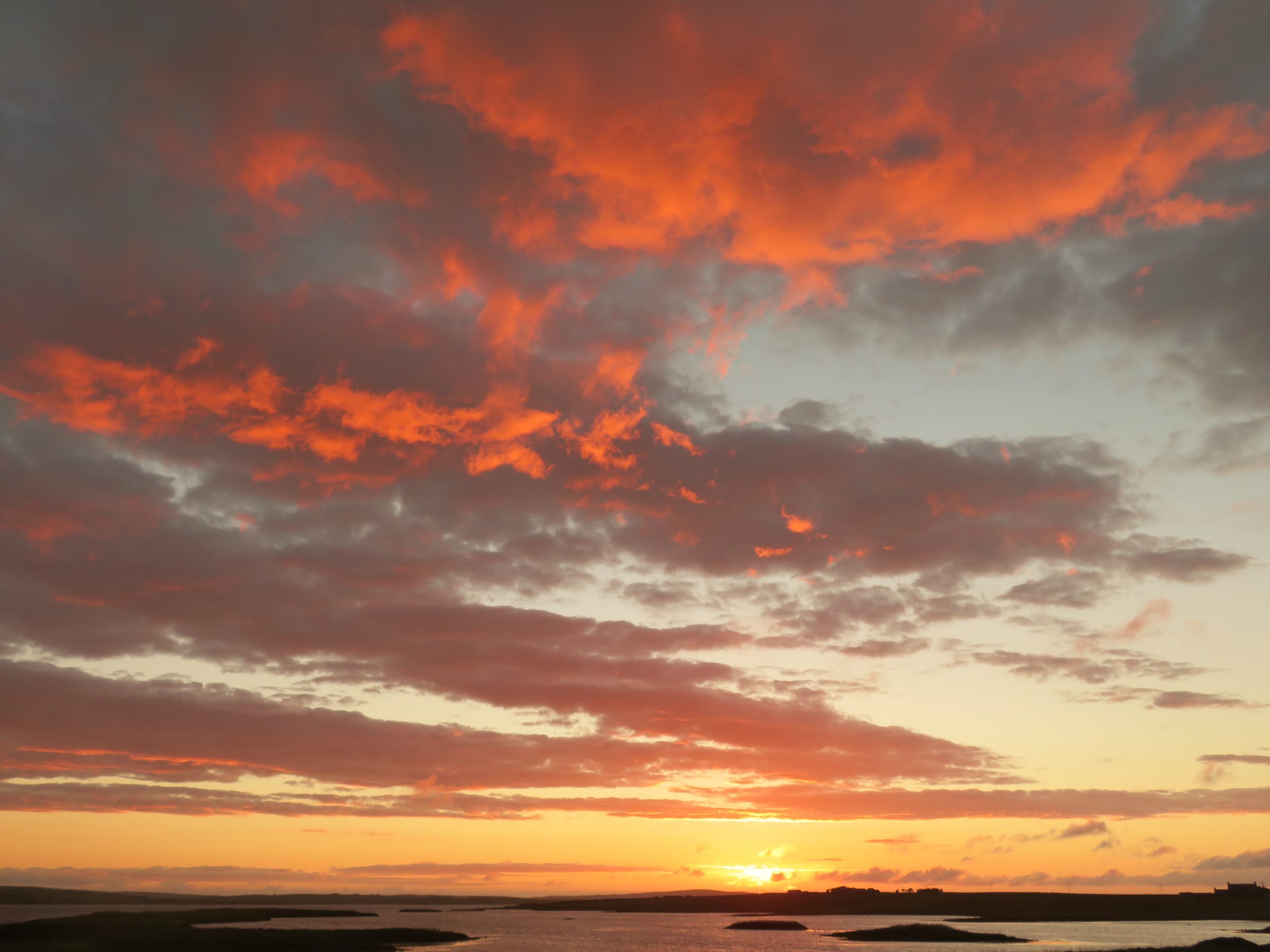 Golden sunset light reflected on the surface of Loch of Harray, the far shore silhouetted against a red sky.