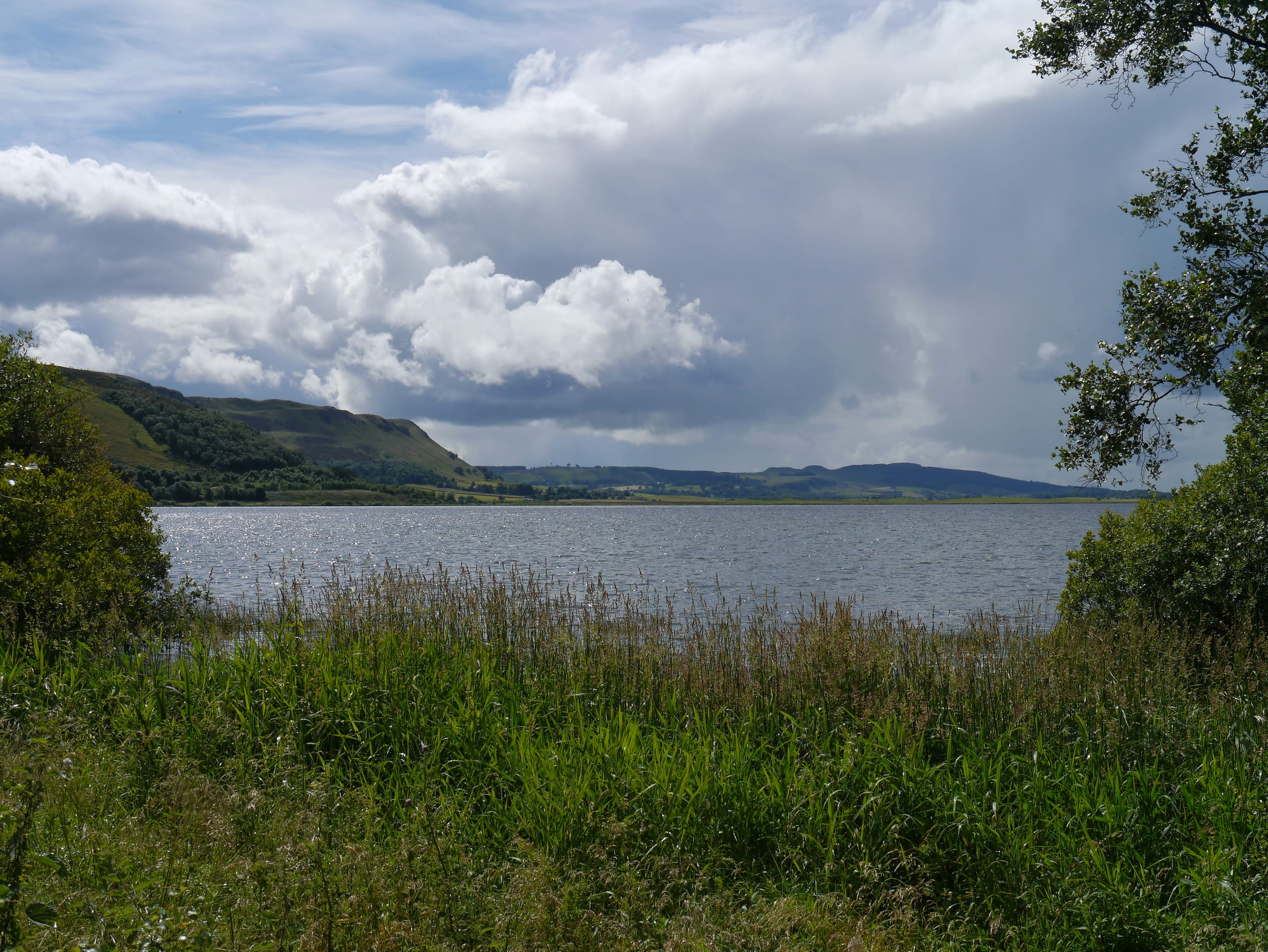 Broad view of Loch Leven from the south shore looking west, loch water filling the middle distance with farmland and hills beyond.