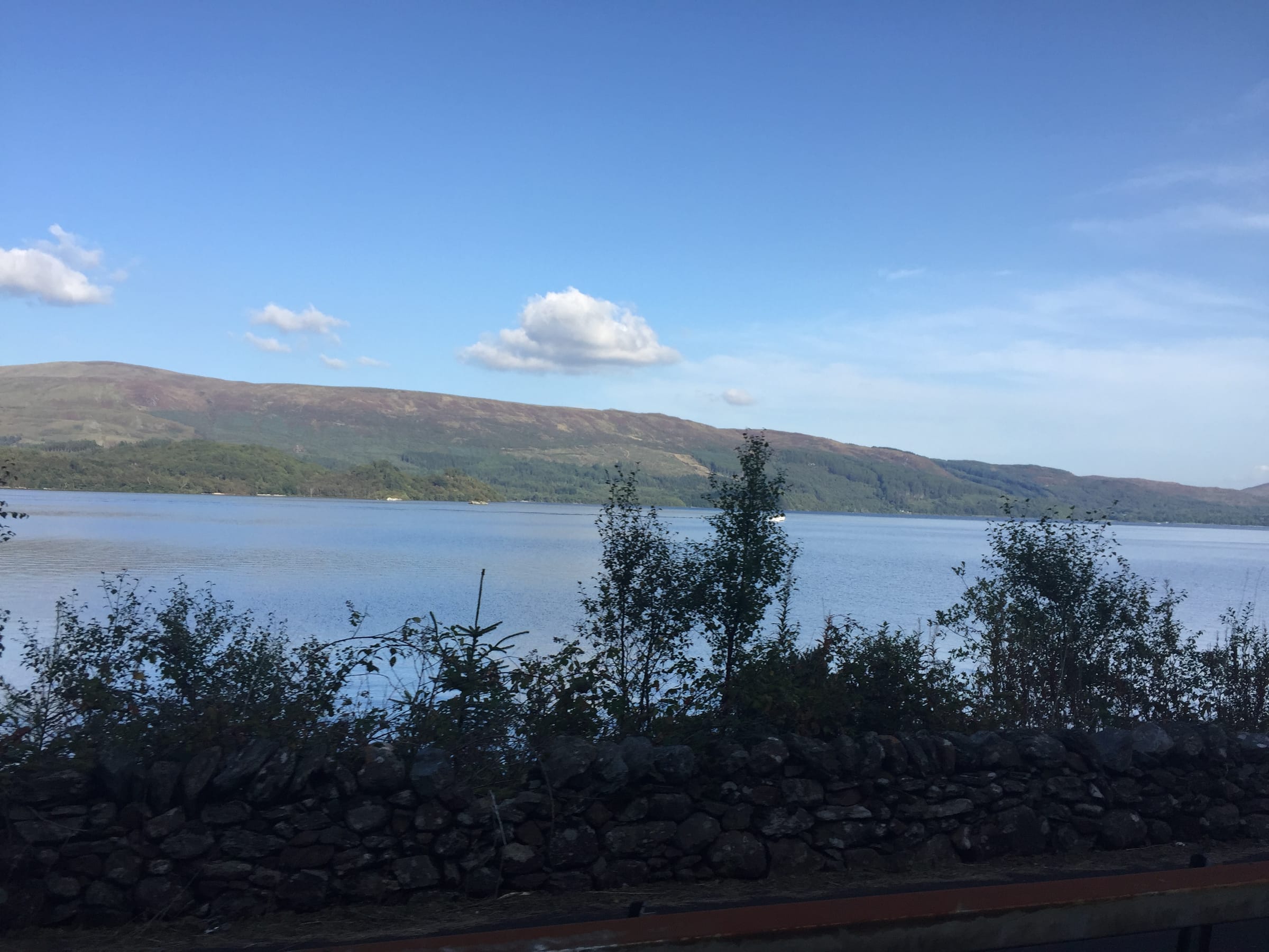 Open water of Loch Lomond north of Luss village, the western shoreline hills reflected in the calm surface.