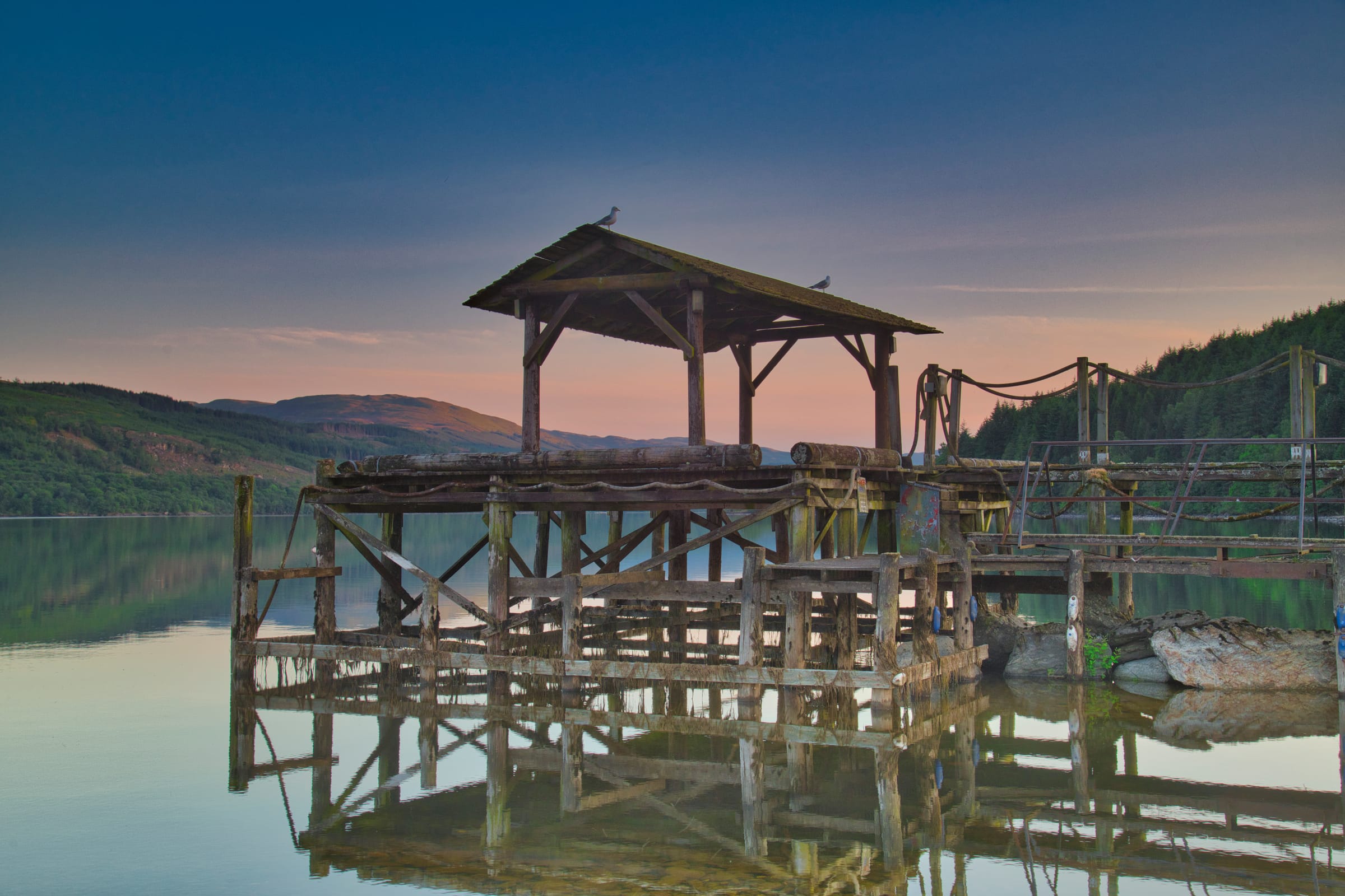 Wide view of Loch Tay at its western end under a golden sunset sky, still water reflecting the evening light.
