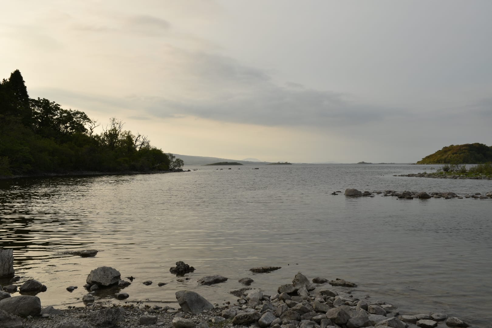 Rocky shoreline of White Island on Lough Mask at evening, calm water reflecting sunset light.