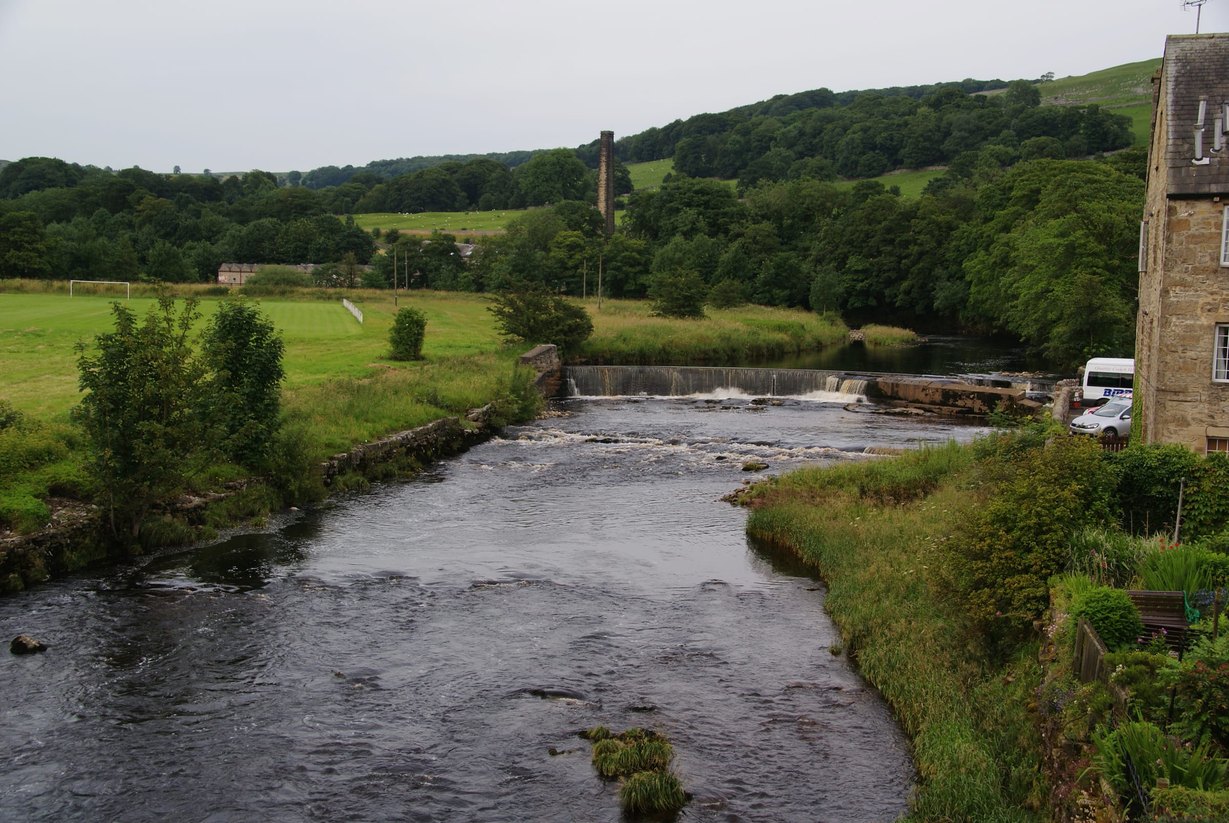 The River Ribble running over limestone ledges and shingle at Settle with the Dales skyline behind.