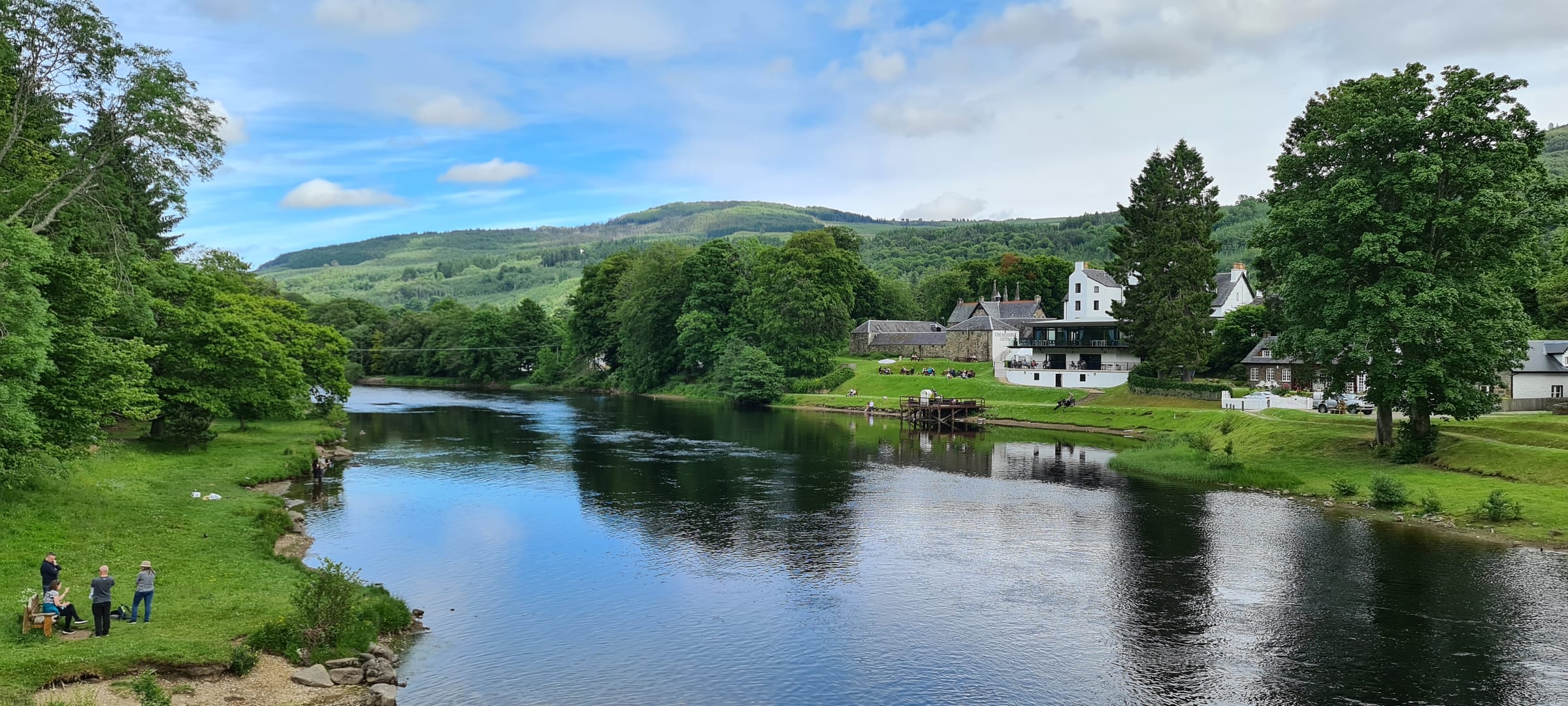 Panoramic view of the River Tay at Kenmore where it exits Loch Tay, with the village and hills beyond.