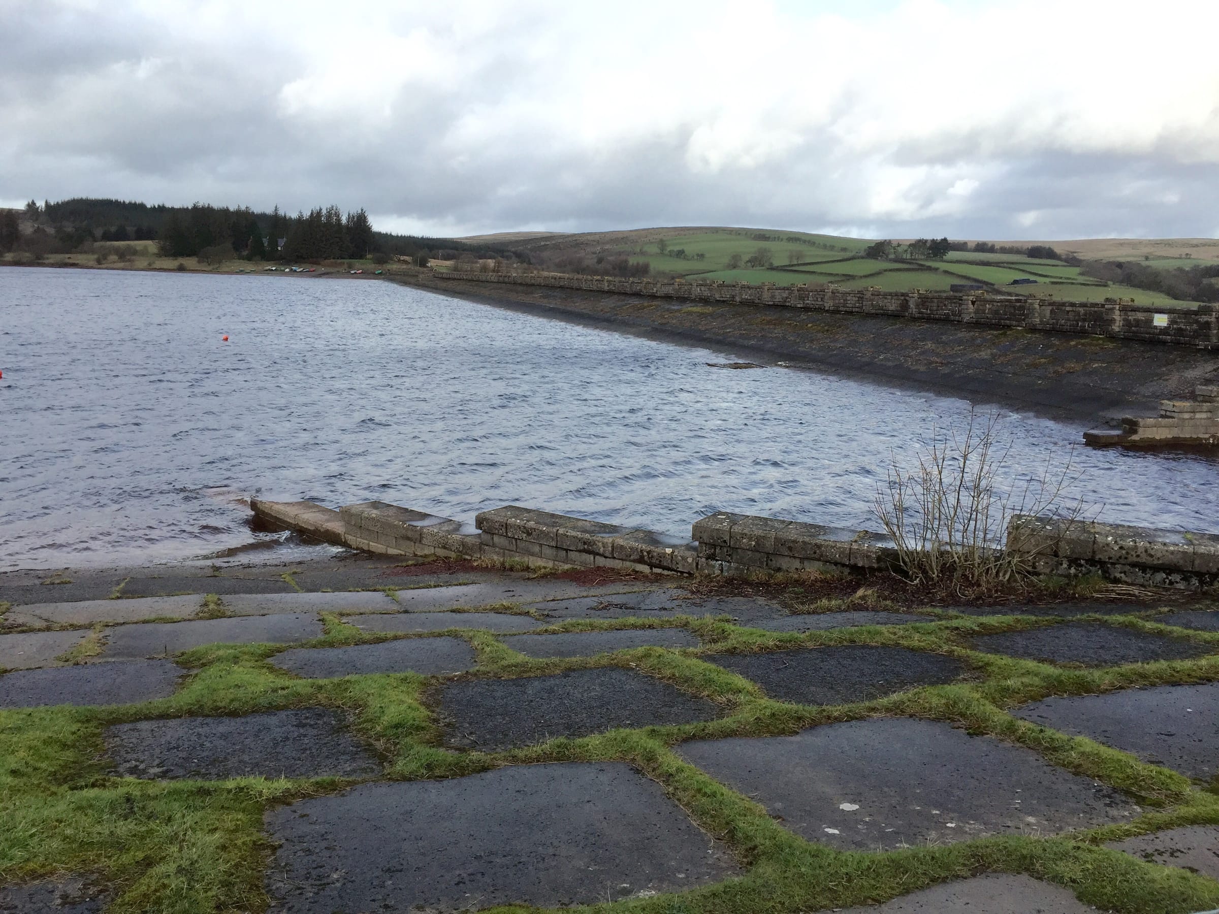 The concrete dam wall at the eastern end of Usk Reservoir with the reservoir water behind the structure.