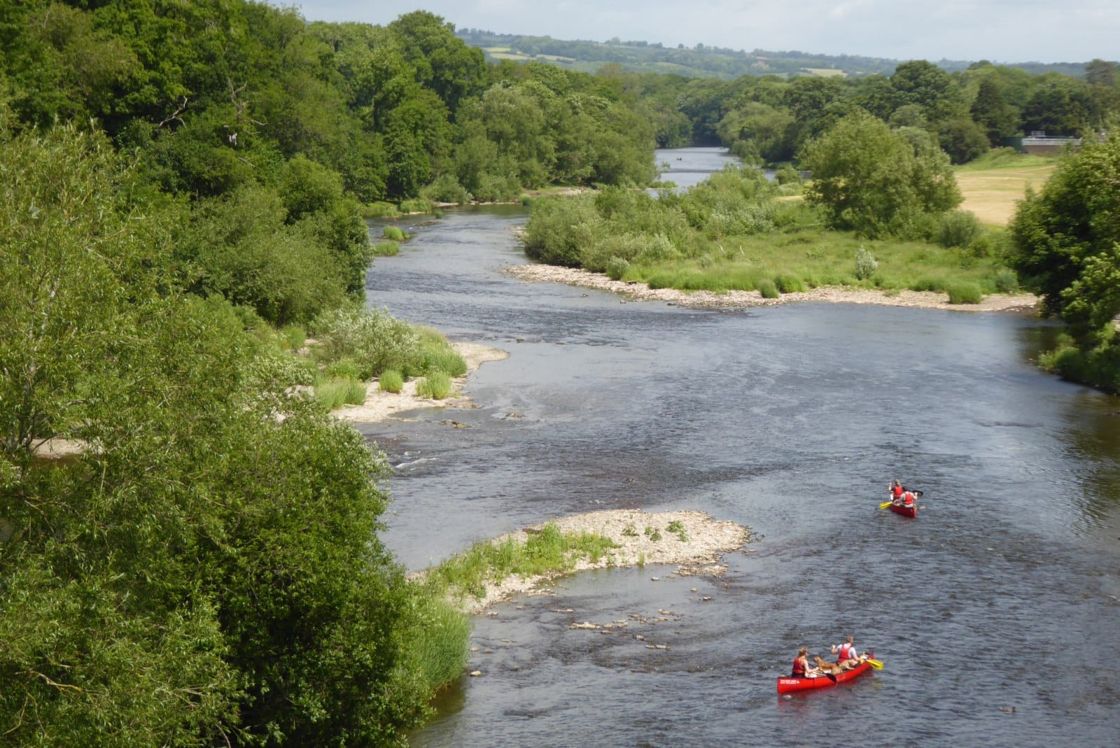 The River Wye at Hay-on-Wye from the bank, broad open water with wooded hills behind, in summer.